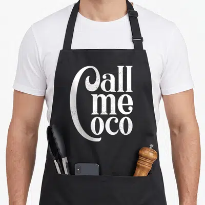 Tablier de cuisine noir avec inscription Call me Coco en lettres blanches style rétro et délavé.