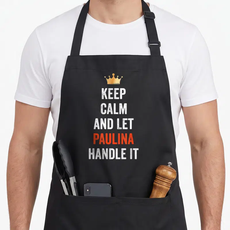 Tablier de cuisine noir avec texte Keep Calm And Let Paulina Handle It et une couronne dorée en haut du motif imprimé.