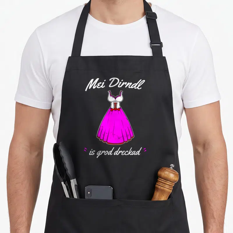 Tablier de cuisine noir avec une illustration de robe rose et le texte Mei Dirndl is grod dreckad en blanc.