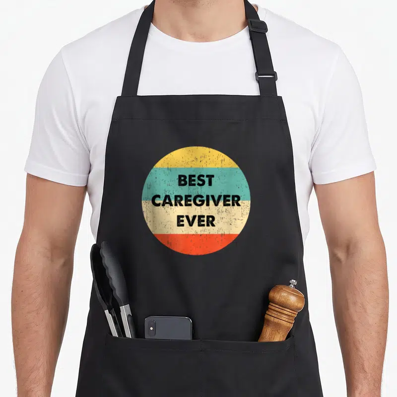 Tablier de cuisine noir avec un motif circulaire retro affichant Best Caregiver Ever en lettres noires.