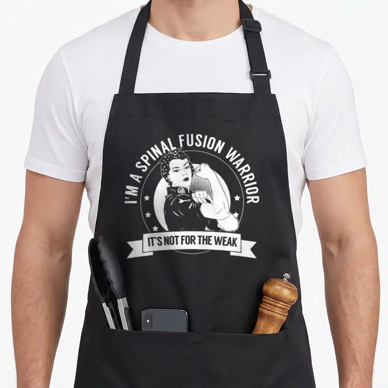 Tablier de cuisine noir avec illustration blanche d'une femme musclée et texte I'm a spinal fusion warrior.