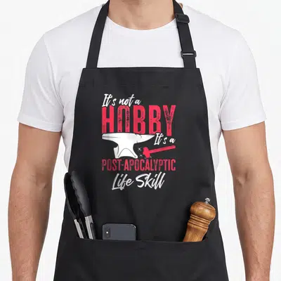 Tablier de cuisine noir avec une enclume blanche, une massue rouge et le texte « It's not a HOBBY It's a POST-APOCALYPTIC Life Skill » en rose et blanc.