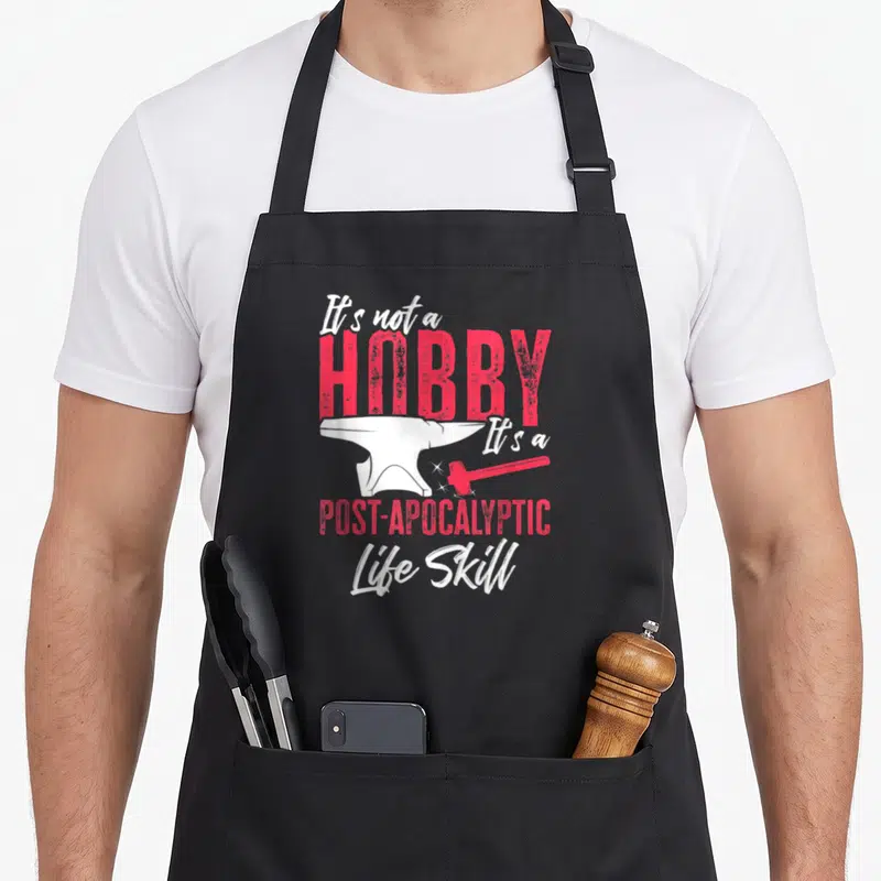 Tablier de cuisine noir avec une enclume blanche, une massue rouge et le texte « It's not a HOBBY It's a POST-APOCALYPTIC Life Skill » en rose et blanc.