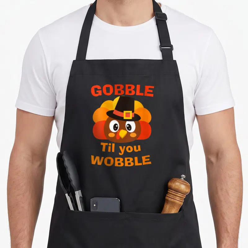 Tablier de cuisine noir avec dindon cartoon portant chapeau et texte Gobble Til You Wobble