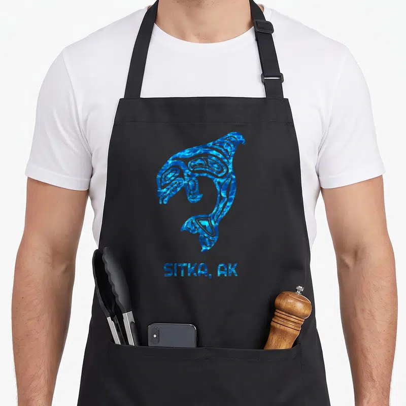 Tablier de cuisine noir avec une orque stylisée en motifs amérindiens bleus et l'inscription SITKA, AK.
