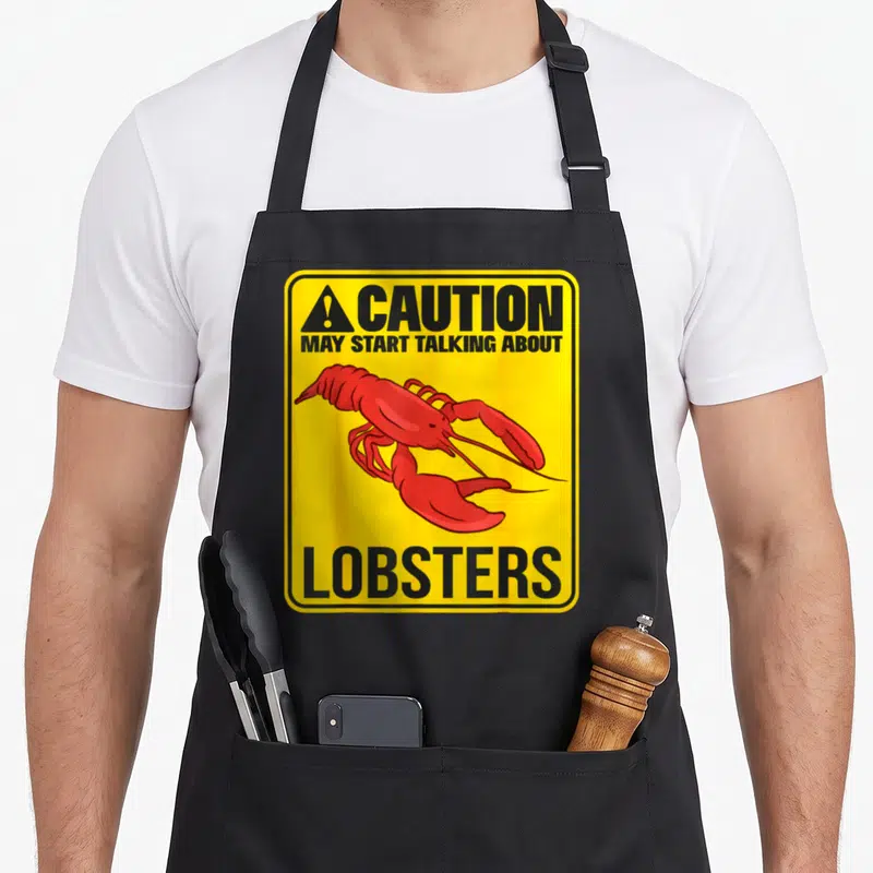Tablier de cuisine noir avec signalisation jaune Caution May Start Talking About Lobsters et homard rouge stylisé.