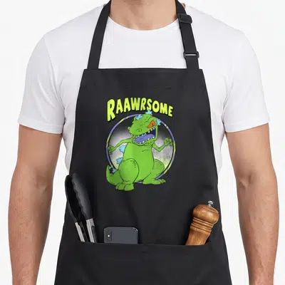Tablier de cuisine noir avec Reptar vert et le texte Raawrsome en lettres jaunes.