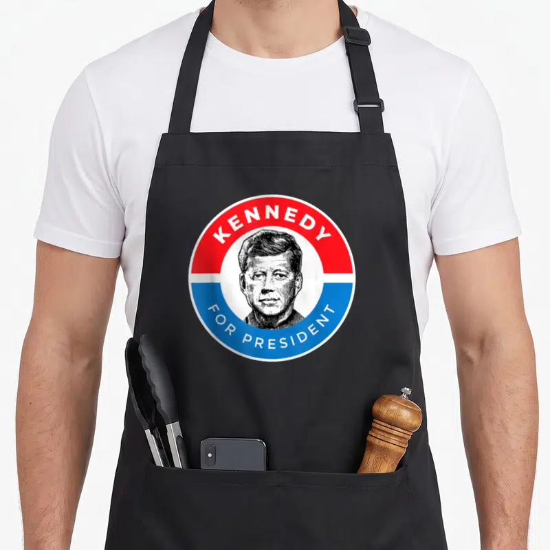 Tablier de cuisine noir avec un logo rond rouge et bleu affichant le portrait de Kennedy et For President.