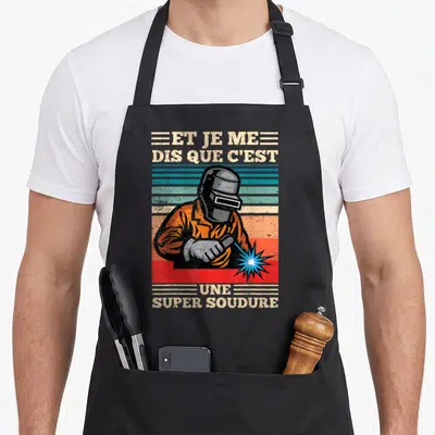 Tablier de cuisine noir avec illustration d'un soudeur en casque et texte humoristique en lettres capitules vintage.