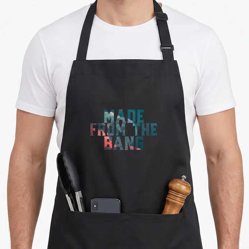 Tablier de cuisine noir avec l'inscription Made From The Bang en lettres colorées sur fond cosmique.