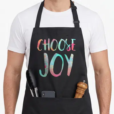 Tablier de cuisine noir avec l'inscription Choose Joy en lettres aquarellées aux teintes pastel vives.