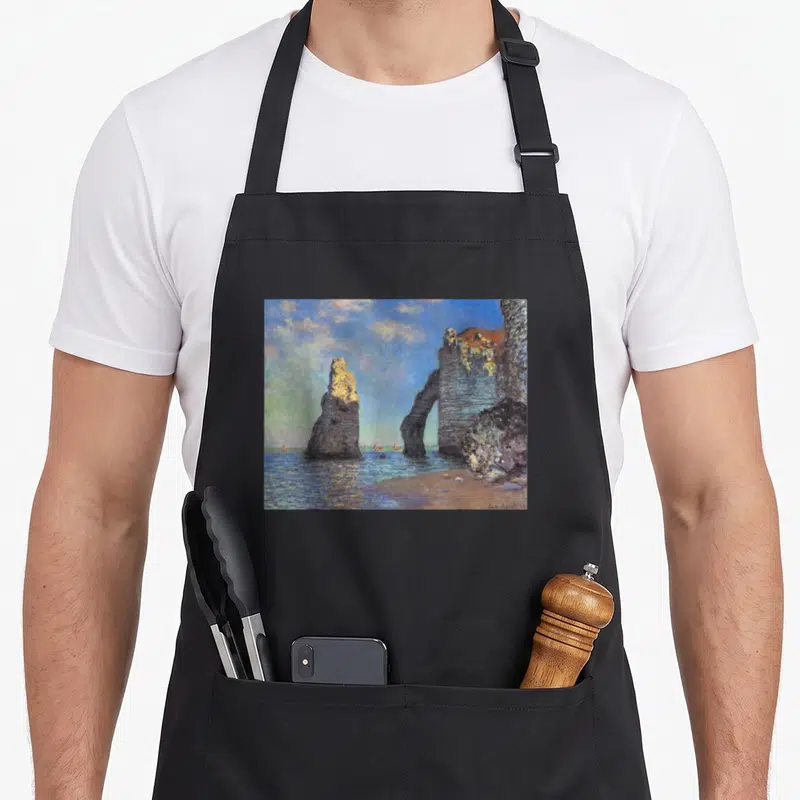 Tablier de cuisine noir avec reproduction des Falaises d'Étretat de Monet imprimée au centre.