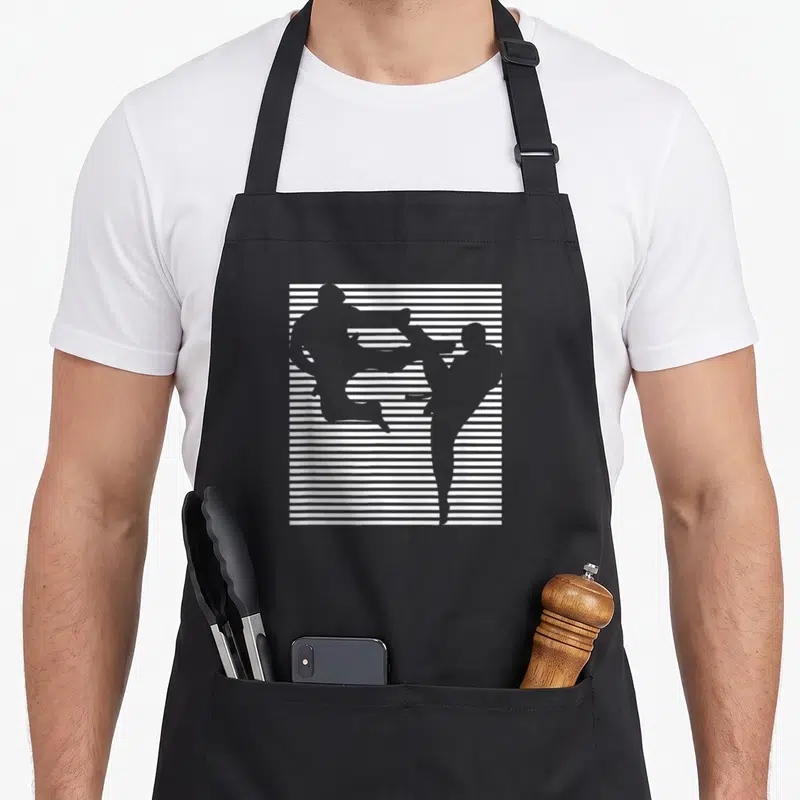 Tablier de cuisine noir avec deux silhouettes grises effectuant des coups de pied sur un fond de bandes blanches horizontales.