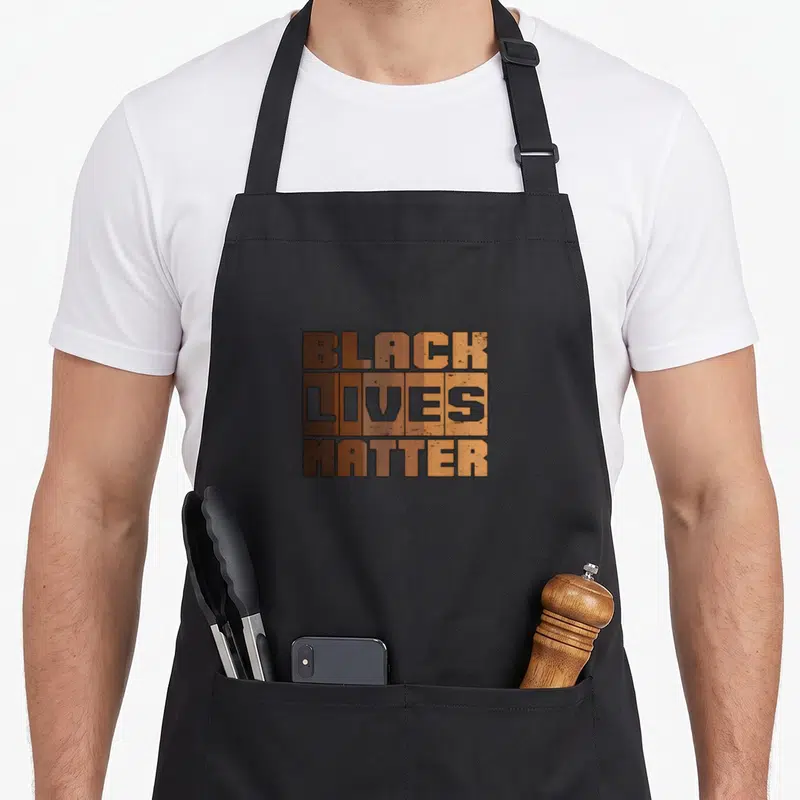 Tablier de cuisine noir avec inscription Black Lives Matter en typographie blocky aux couleurs terreuses.