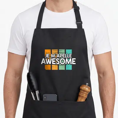 Tablier de cuisine noir avec inscription Je m'appelle Génial sur bandes orange et vertes texturées.