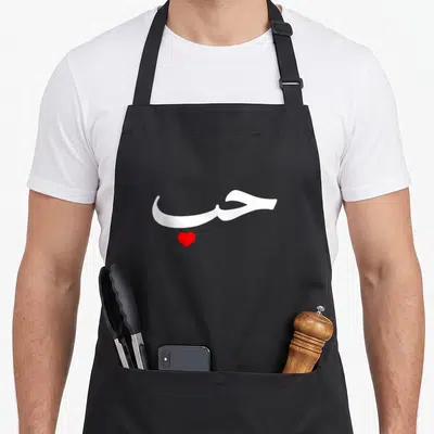 Tablier de cuisine noir avec inscription Love en calligraphie arabe blanche et un petit cœur rouge stylisé au centre.