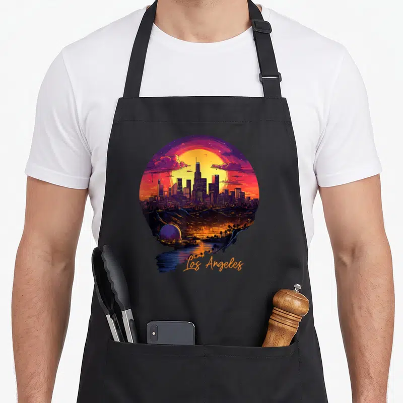 Tablier de cuisine noir avec illustration circulaire du skyline de Los Angeles au coucher de soleil et texte Los Angeles en bas.
