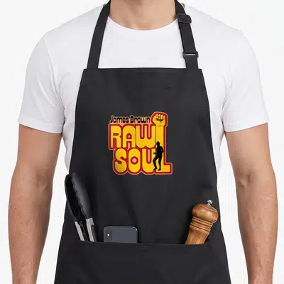 Tablier de cuisine noir avec le logo James Brown Raw Soul Fist en jaune et rouge incluant un poing levé et une silhouette.