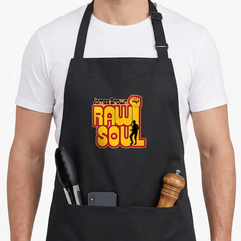 Tablier de cuisine noir avec le logo James Brown Raw Soul Fist en jaune et rouge incluant un poing levé et une silhouette.