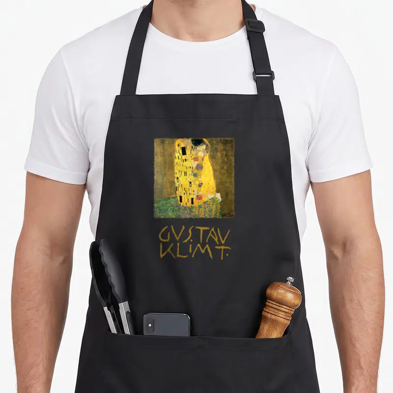 Tablier de cuisine noir avec reproduction du Kiss de Gustav Klimt et signature dorée en dessous.