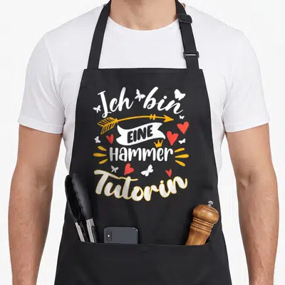 Tablier de cuisine noir avec une flèche dorée, des cœurs rouges et le texte Eine Hammer Tutorin en typographie blanche.