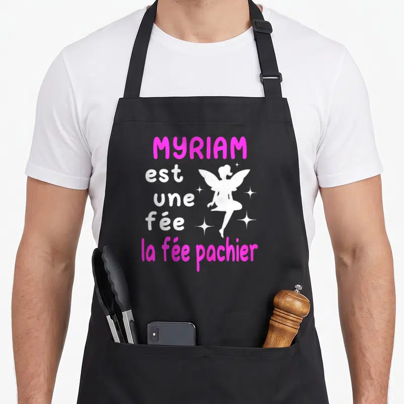 Tablier de cuisine noir avec le texte Myriam est une fée la fée pachier et une silhouette de fée blanche entourée d'étoiles.