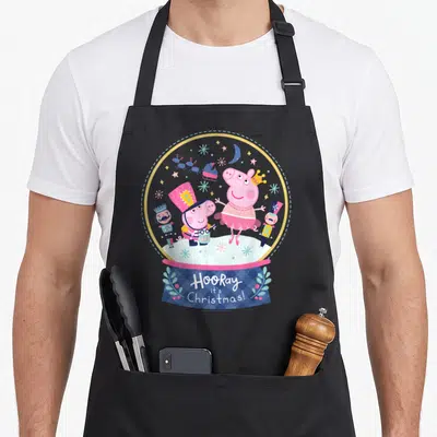 Tablier de cuisine noir avec une illustration colorée de Peppa Pig dans une boule de neige festive entourée de soldats de bois.