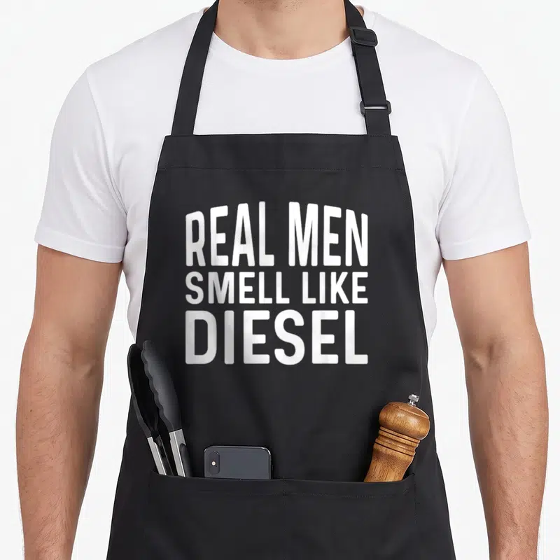 Tablier de cuisine noir avec l'inscription blanche Les vrais hommes sentent le diesel en gros caractères gras.