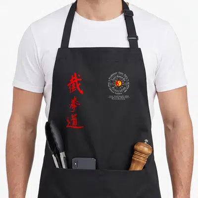 Tablier de cuisine noir avec calligraphie rouge verticale et logo circulaire blanc du Just Kune Do Association au centre droit.