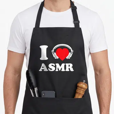 Tablier de cuisine noir avec le texte I Love ASMR et des écouteurs blanc entourant un cœur rouge vif au centre du torse.