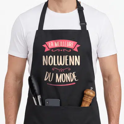 Tablier de cuisine noir avec l'inscription La meilleure Nolwenn du monde en rose et crème.