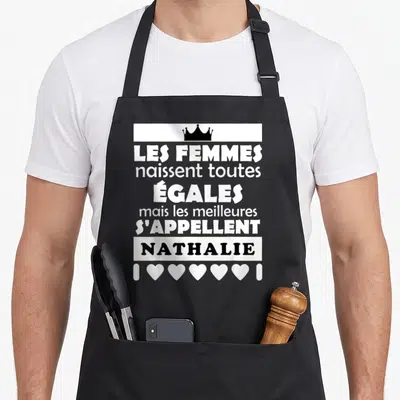 Tablier de cuisine noir avec inscription blanche Les femmes naissent toutes égales mais les meilleures s'appellent Nathalie surplombée d'une couronne.