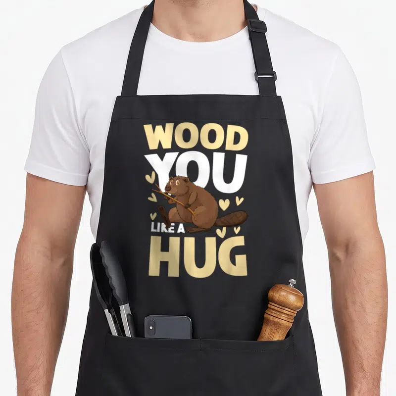 Tablier de cuisine noir avec illustration d'un castor tenant des branches et texte Wood You Like A Hug.