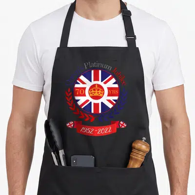 Tablier de cuisine noir orné d'un blason circulaire au drapeau britannique et d'une couronne dorée.