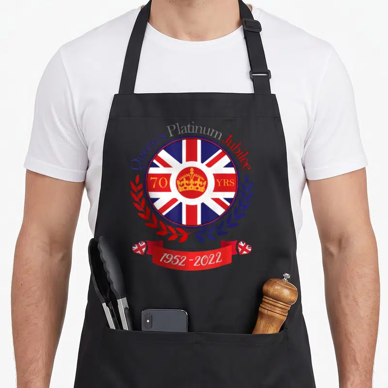 Tablier de cuisine noir orné d'un blason circulaire au drapeau britannique et d'une couronne dorée.