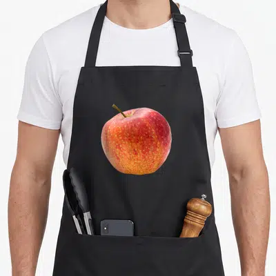Tablier de cuisine noir avec une grande pomme rouge et jaune imprimée au centre, réalistes sur la peau du fruit.