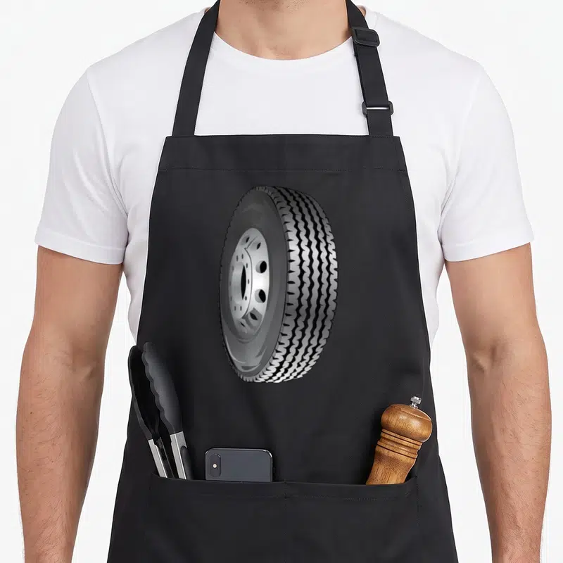 Tablier de cuisine noir avec une grande roue de véhicule heavy weight imprimée au centre du vêtement.