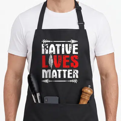 Tablier de cuisine noir avec inscription Native Lives Matter encadrée par deux flèches et une plume centrale.