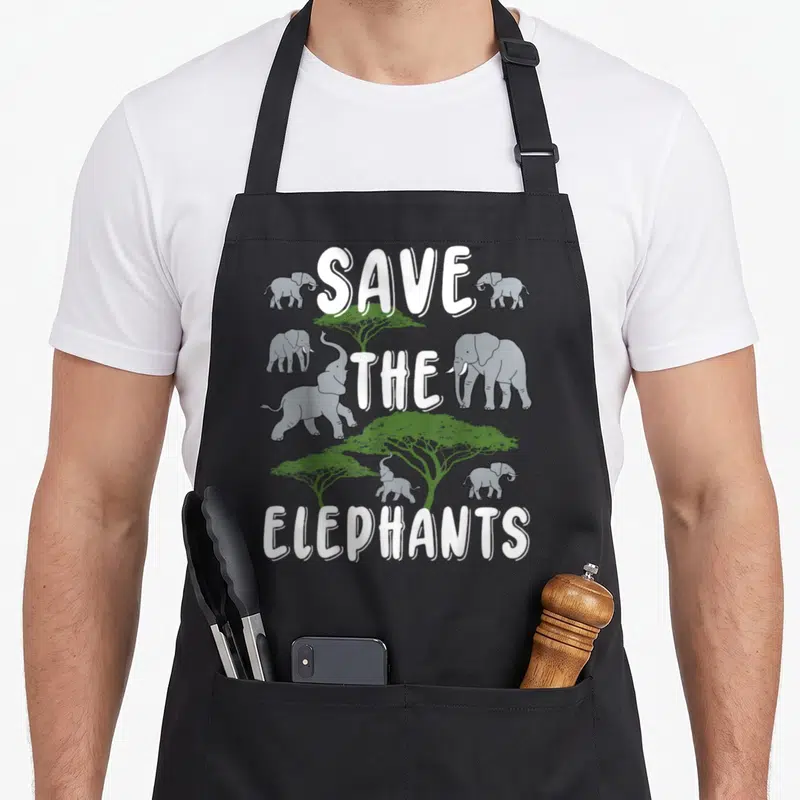 Tablier de cuisine noir avec inscription Save The Elephants et dessins d'éléphants gris entourés d'arbres verts.