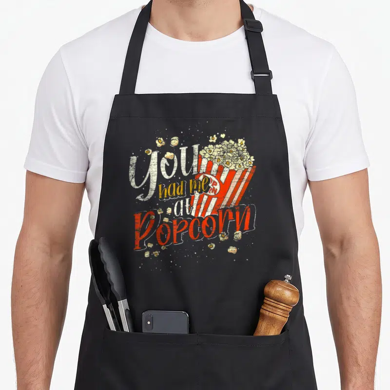 Tablier de cuisine noir avec l'inscription Tu M'As Eu Au Popcorn et une barquette de popcorn vintage.