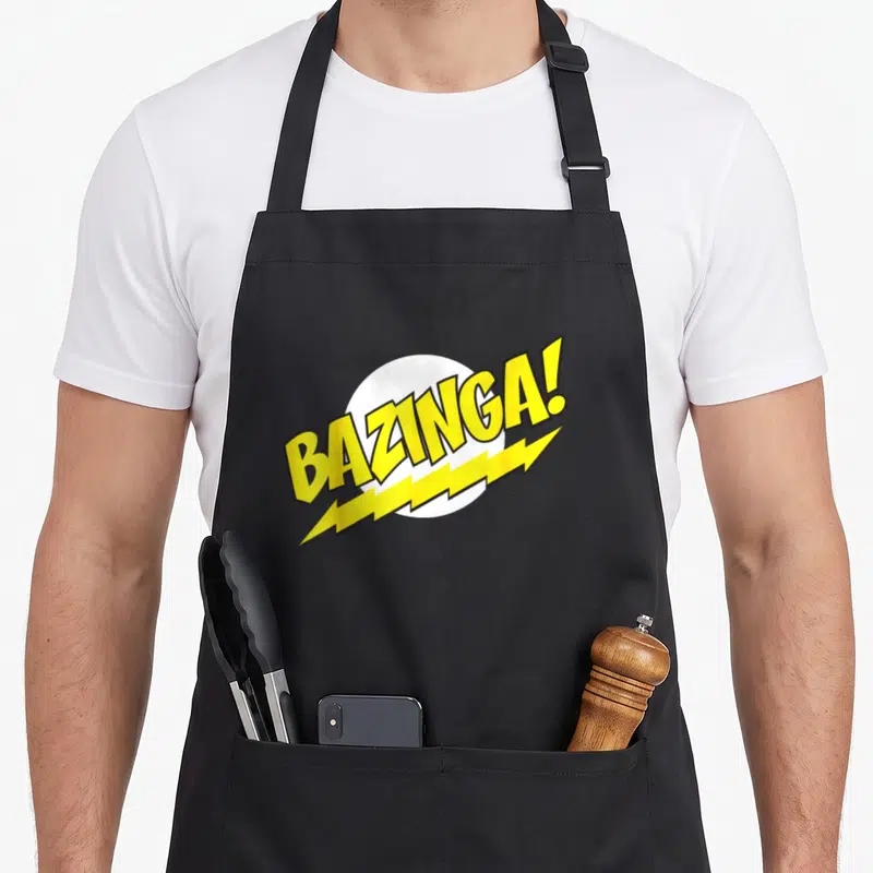 Tablier de cuisine noir avec le logo Bazinga. en lettres jaunes stylisées et un éclair sous-jacent.