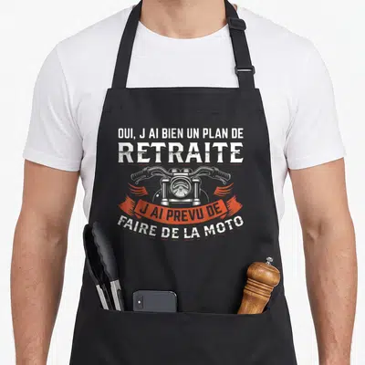 Tablier de cuisine noir avec illustration de guidon moto et texte humoristique sur la retraite en blanc et orange.