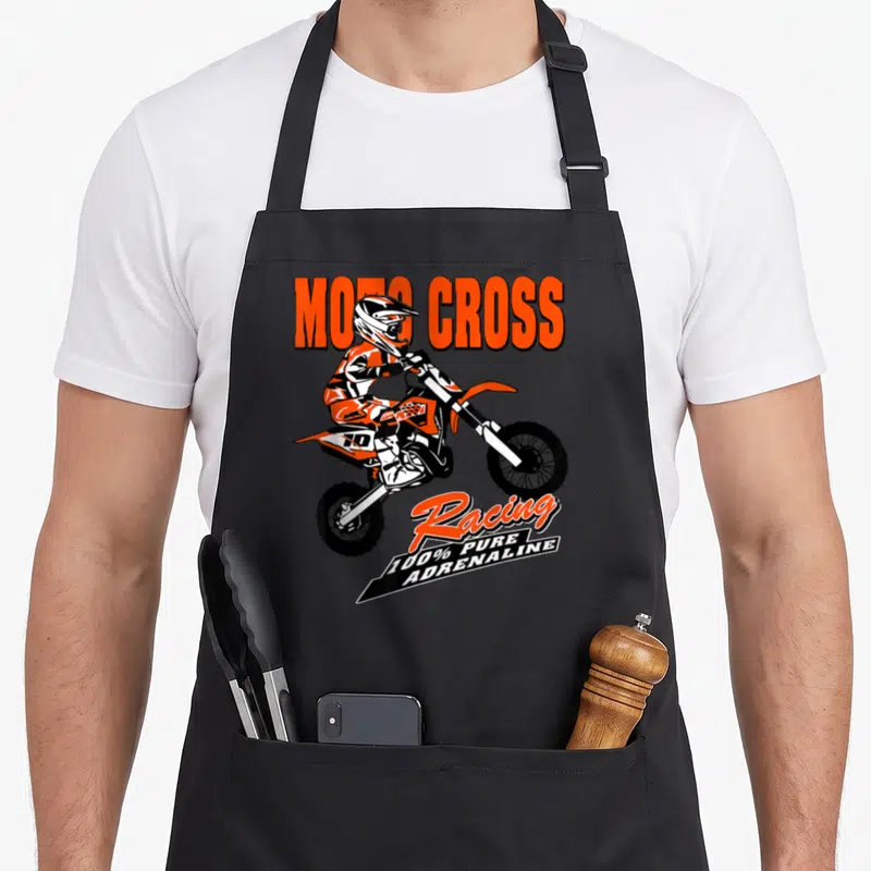 Tablier de cuisine noir avec illustration d'un pilote de moto cross effectuant un saut et du texte orange et blanc.