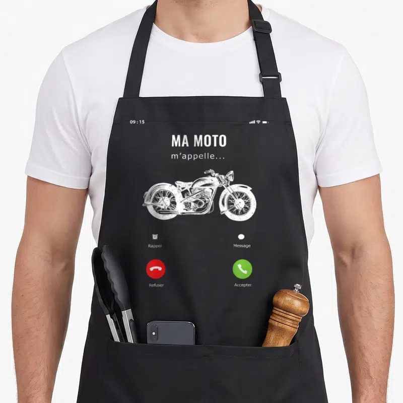 Tablier de cuisine noir avec un écran de téléphone affichant Ma Moto m'appelle et un dessin de moto vintage en blanc.