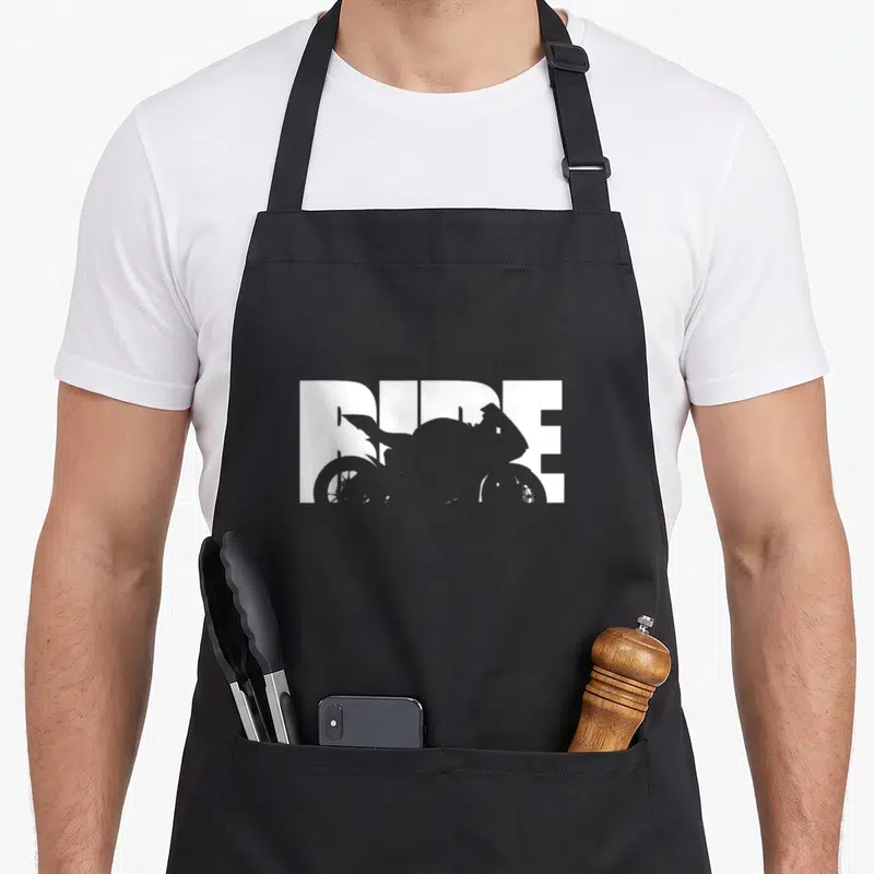 Tablier de cuisine noir avec le mot Ride en blanc et une silhouette de moto sportive intégrée au texte.