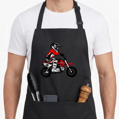 Tablier de cuisine noir avec une illustration colorée d'un enfant pilotant une moto cross rouge et blanche portant le numéro 8.