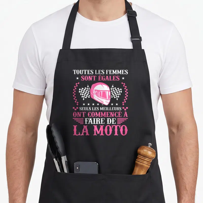 Tablier de cuisine noir avec casque de moto rose, drapeaux à carreaux et texte blanc sur fond uni.