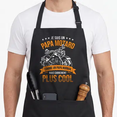 Tablier de cuisine noir avec inscription Papa Motard et illustration de moto cruiser en blanc et orange.