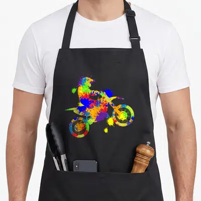 Tablier de cuisine noir avec une enduro supermoto aux éclats de peinture multicolores et un pilote en action.