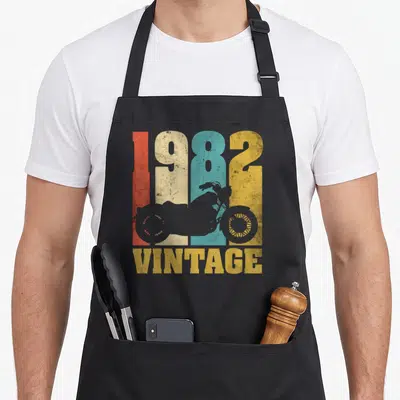 Tablier de cuisine noir avec inscription 1982 vintage et silhouette de moto retro multicolore.